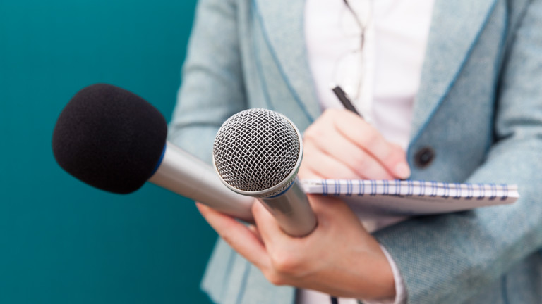 Female journalist at press conference, writing notes, holding microphone